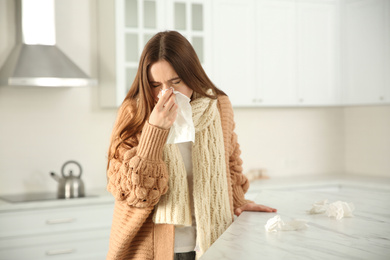 Sick young woman sneezing in kitchen. Influenza virus