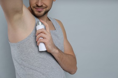 Photo of Man applying deodorant on grey background, closeup. Space for text