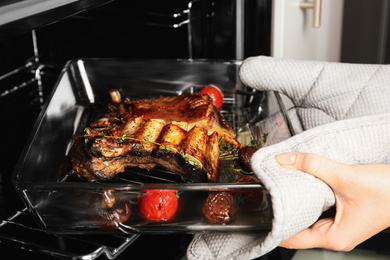 Woman taking delicious roasted ribs out of oven, closeup