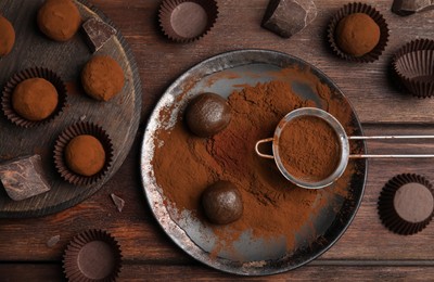 Delicious chocolate truffles powdered with cocoa on wooden table, flat lay