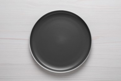 New dark plate on white wooden table, top view