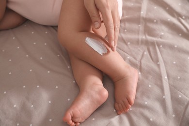 Mother applying moisturizing cream onto her little baby's skin on bed, closeup