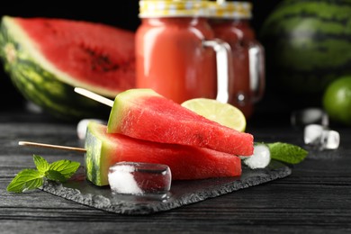 Slate board with juicy watermelon, ice and lime on black wooden table, closeup