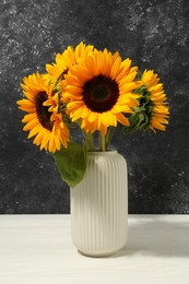 Photo of Vase with beautiful sunflowers on white table against black background