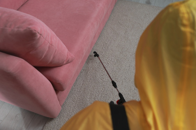 Pest control worker in protective suit spraying insecticide near sofa indoors, above view