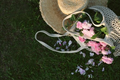 Photo of Straw hat and mesh bag with beautiful tea roses on green grass outdoors, flat lay. Space for text