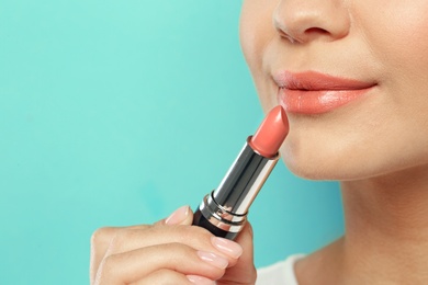 Beautiful woman applying nude lipstick on color background, closeup. Space for text