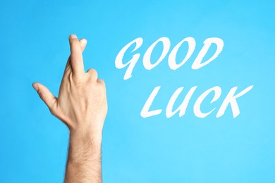 Man with crossed fingers on light blue background, closeup. Good luck superstition