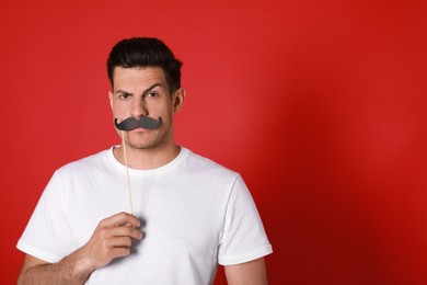 Photo of Funny man with fake mustache on red background. Space for text