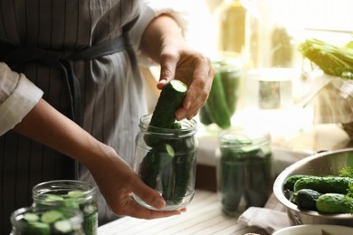 Photo of Woman putting cucumbers into jar in kitchen, closeup. Canning vegetables