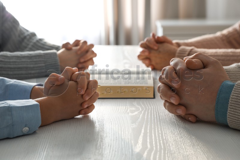 Boy and his godparents praying together at white wooden table indoors, closeup