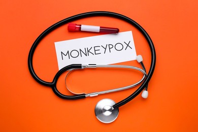 Word Monkeypox, stethoscope and test tube with blood sample on orange background, flat lay