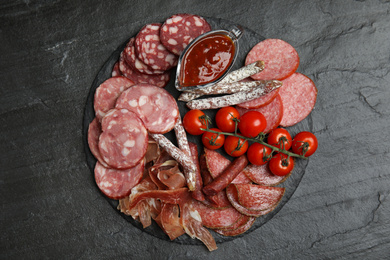 Different types of sausages with tomatoes served on black table, flat lay