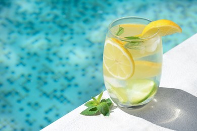 Refreshing water with lemon slices and mint near swimming pool, closeup. Space for text