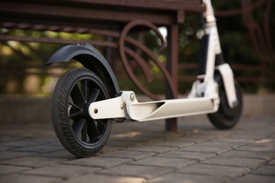 Photo of Modern electric kick scooter near bench in park, closeup
