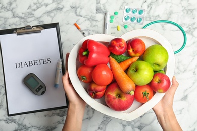 Woman holding tray with fruits and vegetables over table, top view. Diabetes diet