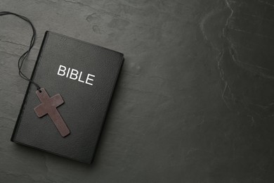 Christian cross and Bible on black table, top view. Space for text