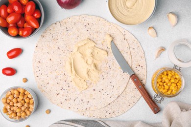 Photo of Tortilla with hummus and vegetables on light table, flat lay