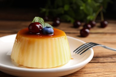 Photo of Plate of delicious caramel pudding with blueberry, cherry and mint served on wooden table, closeup