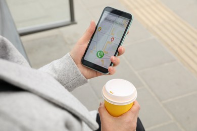 Woman with cup of coffee ordering taxi on her smartphone outdoors, closeup