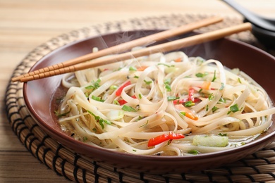 Photo of Plate of hot noodles with broth, vegetables and chopsticks on table, closeup