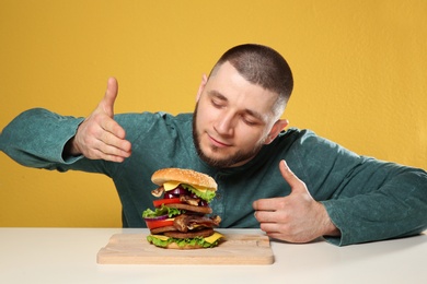 Photo of Young man with tasty huge burger at table