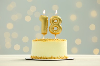 Photo of Coming of age party - 18th birthday. Delicious cake with number shaped candles on white table against blurred lights