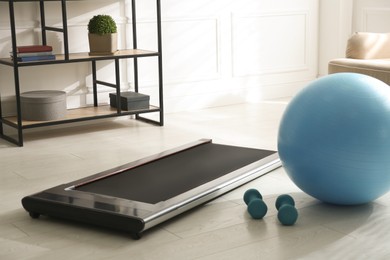 Modern walking treadmill, dumbbells and fitness ball in living room. Home gym equipment