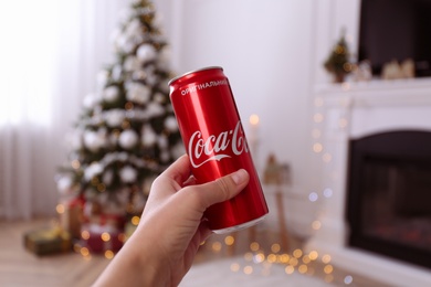 Photo of MYKOLAIV, UKRAINE - JANUARY 13, 2021: Woman holding can of Coca-Cola in room with Christmas tree, closeup