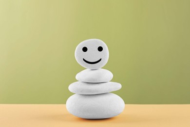 Stack of stones with drawn happy face on beige table against light green background. Zen concept