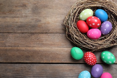 Colorful eggs and nest on wooden background, flat lay with space for text. Happy Easter