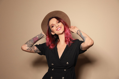 Beautiful woman with tattoos on arms against beige background