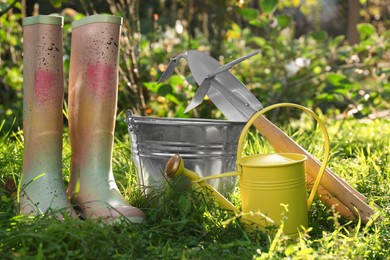 Photo of Watering can, gardening tools and rubber boots on green grass outdoors