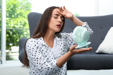 Woman with portable fan suffering from heat at home. Summer season