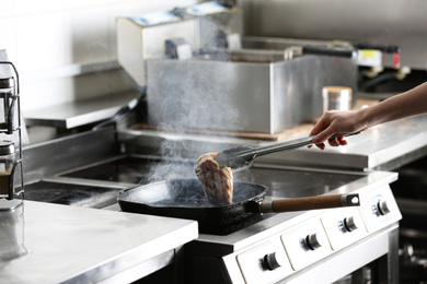 Female chef cooking chicken fillet on stove in restaurant  kitchen, closeup