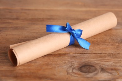 Rolled student's diploma with blue ribbon on wooden table