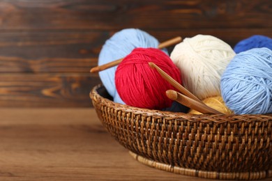 Wicker basket with clews of colorful knitting threads and crochet hooks on wooden table, closeup. Space for text