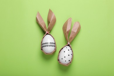 Photo of Easter bunnies made of craft paper and eggs on light green background, flat lay