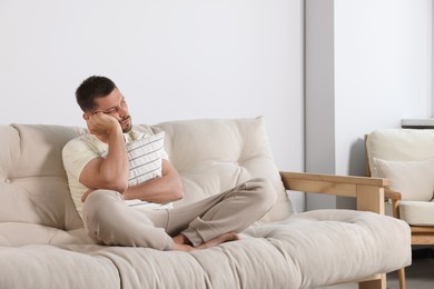 Photo of Sleepless man hugging pillow on sofa at home