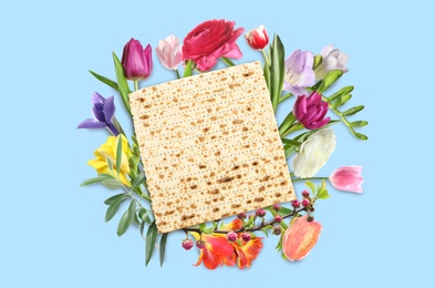 Tasty matzo and flowers on blue background, flat lay. Passover (Pesach) celebration