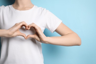 Woman making heart with hands on light blue background, closeup. Space for text