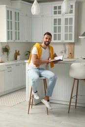 Handsome man with book sitting on stool in kitchen