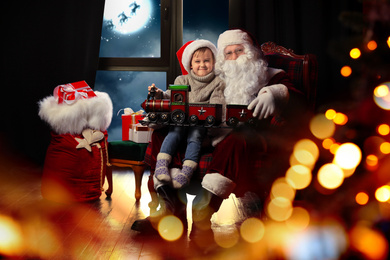Image of Santa Claus and little boy with toy train near window at home. Christmas holiday