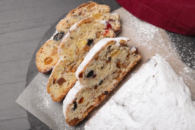 Traditional Christmas Stollen with icing sugar on black table, flat lay