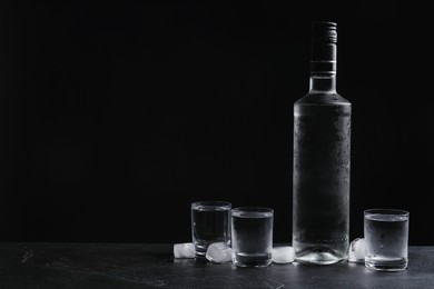 Bottle of vodka and shot glasses with ice on table against black background. Space for text