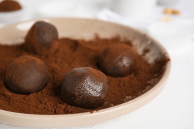 Plate with delicious chocolate truffles and cocoa powder on white table, closeup