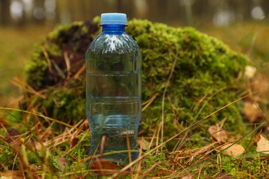 Photo of Plastic bottle of fresh water on ground in forest