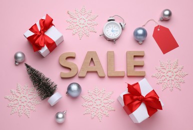 Word Sale made of wooden letters, gift boxes, alarm clock and Christmas decorations on pink background, flat lay