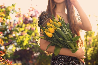 Teenage girl with bouquet of yellow tulips in park on sunny day, closeup. Space for text