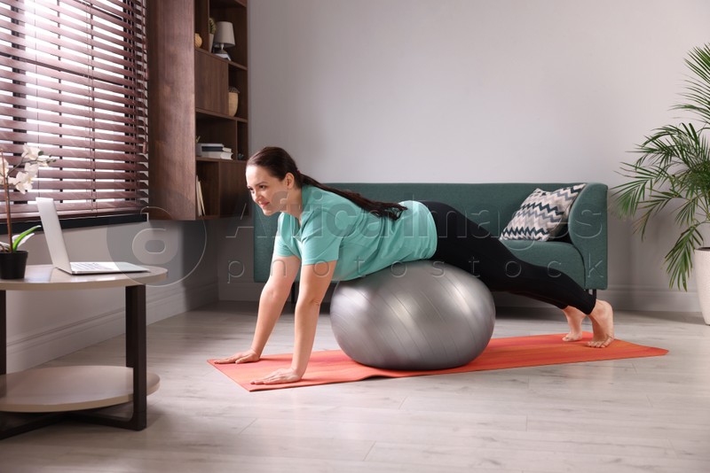 Photo of Overweight woman doing exercise with fitness ball while watching online class at home